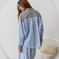 A woman wearing a light blue striped pajama shirt with black and white checkered accents in a dressing gown plaid style