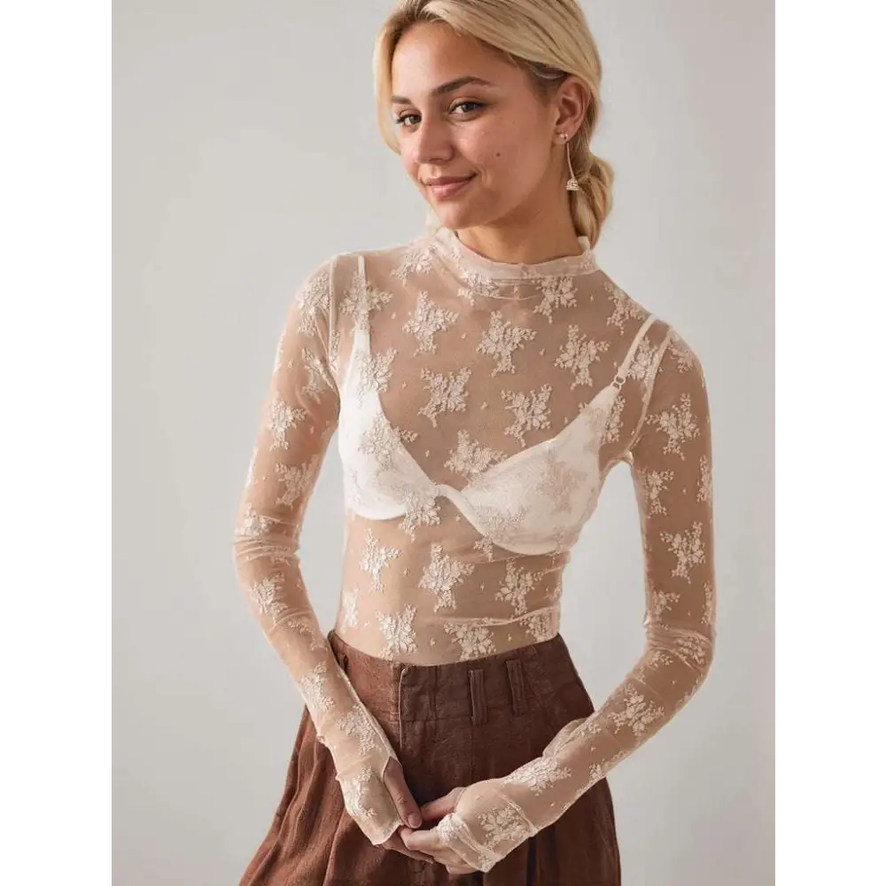 Women’s sheer beige long-sleeved see-through lace floral mesh top with high neckline and white bralette underneath