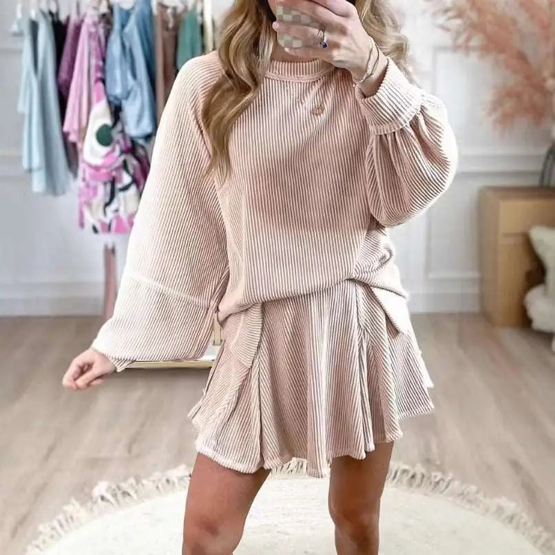 A soft blush pink women’s solid colour ribbed knit casual suit with a loose top and flared skirt tied at the waist