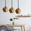 Three geometric wood pendant lights with a warm natural finish and edison glass bulbs hang above a living room table