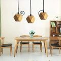 Three geometric wood pendant lights with edison glass bulbs and a warm natural finish hang above a dining table
