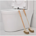 Two wooden household handle cleaning toilet brushes with beige plastic heads and natural bristles leaning on white toilet
