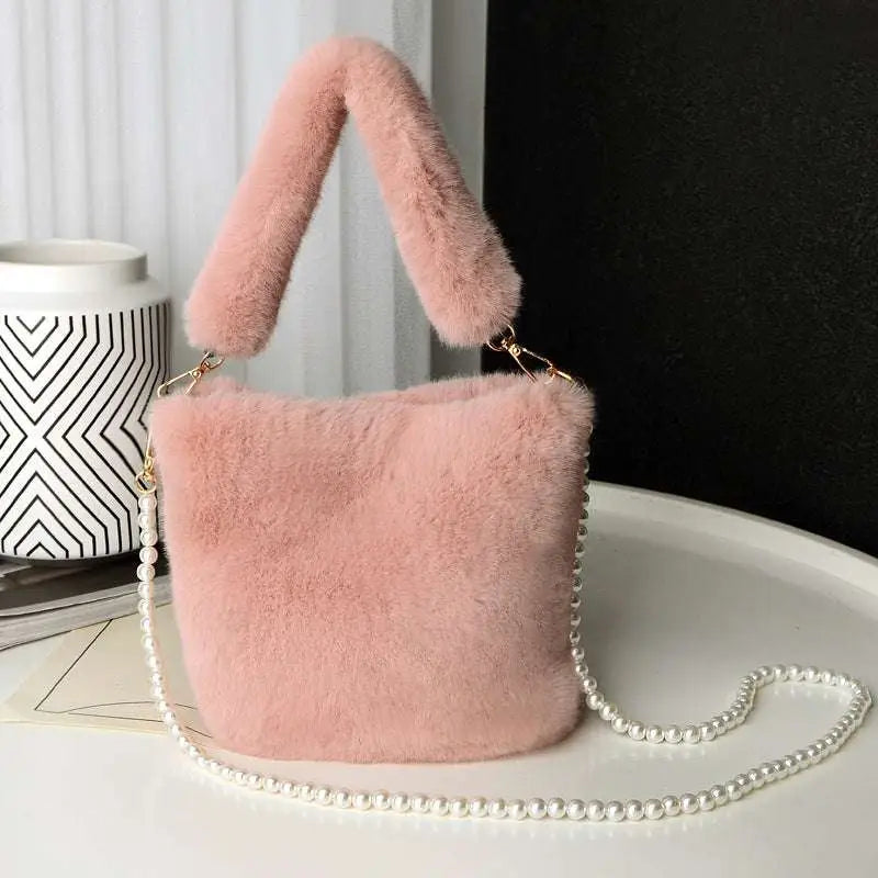 Soft pink plush bucket bag with checkerboard plush design, fuzzy handle, and delicate pearl chain strap