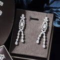 A pair of elegant silver zircon necklace earrings with floral tops, emerald-cut stones, diamonds, and teardrop pendants